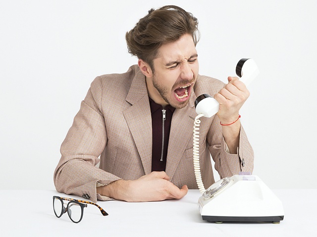 bilden visar en man som skriker mot en telefonlur och ser arg ut