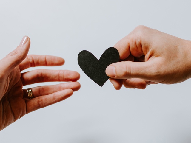 Bilden visar två händer där en hand ger ett svart hjärta till någon annans hand