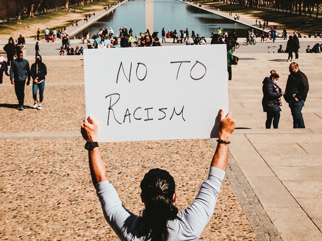 Bilden visar en person som håller i en skylt där det står "nej till rasism"