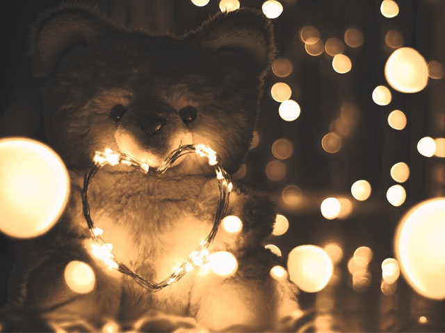 Bilden visar en nallebjörn som håller i ett hjärta format av en ljusslinga med små lampor runtom i bilden