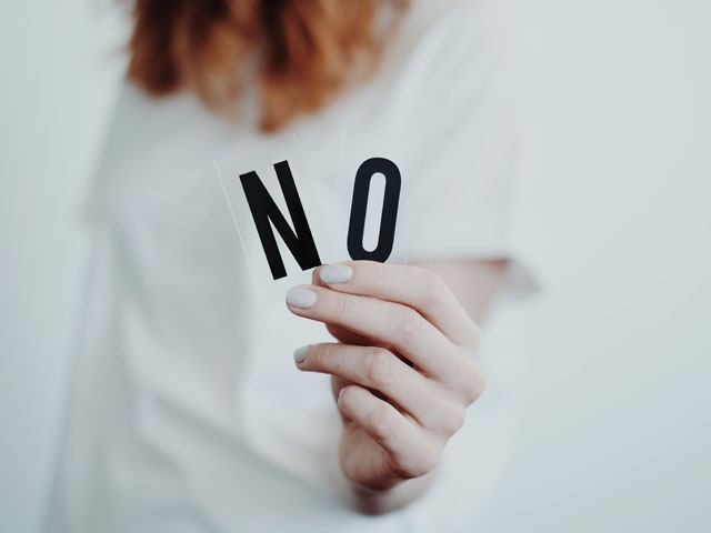 Bilden visar en person lutad framåt som håller i två svarta bokstäver, "NO"