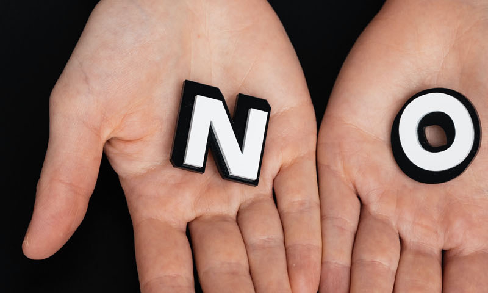 Bilden visar två händer på en svar bakgrund där händer har bokstäverna "NO"