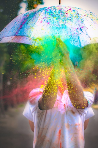 Person håller paraply som skydd mot färg i alla regnbågens färger som kommer mot hen
