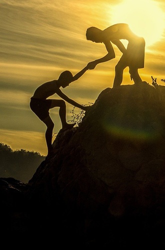 Bilden visar en person som sträcker ut handen till en annan och hjälper hen att komma upp på ett berg