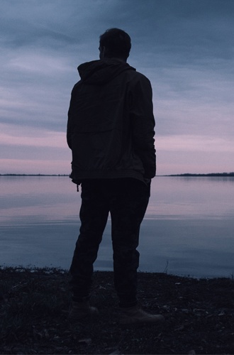 Bilden visar en mörk profil av en man som står och tittar ut mot en sjö