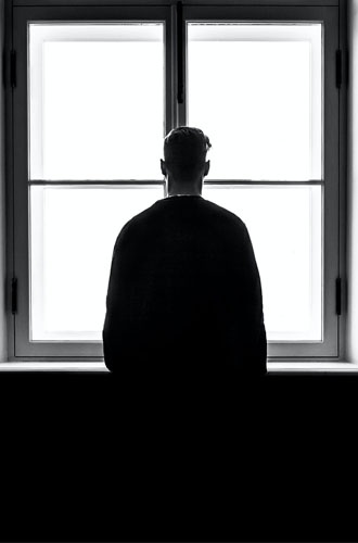Bilden är svart och vit med en person som tittar ut ur ett fönster